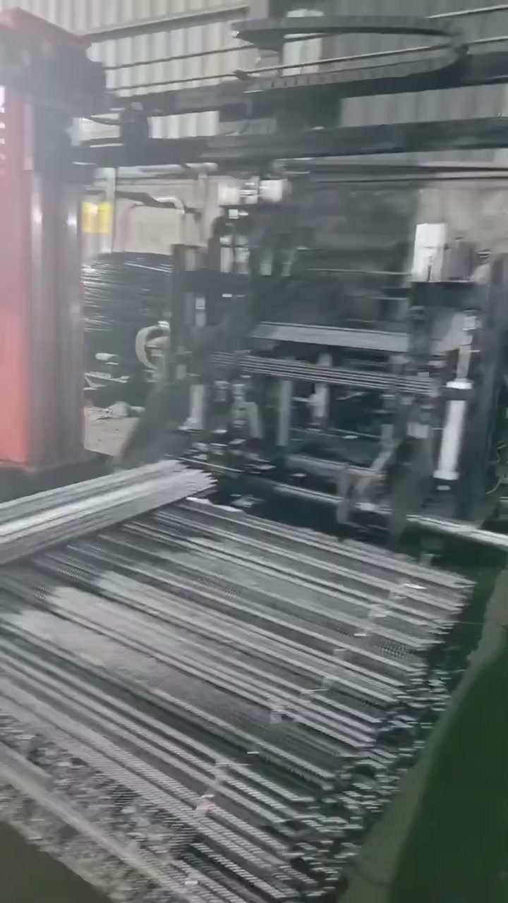 A bundle of ribbed steel bars lying horizontally under the frame and arms of an automatic tying machine