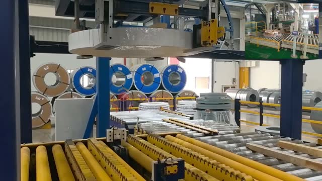 Портальный захват поднимает медную катушку между двумя роликовыми конвейерами на линии по перемещению катушек.