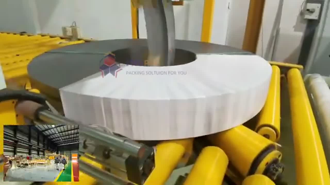 Steel coil on a rotating platform with yellow rollers and a machine arm positioned above it