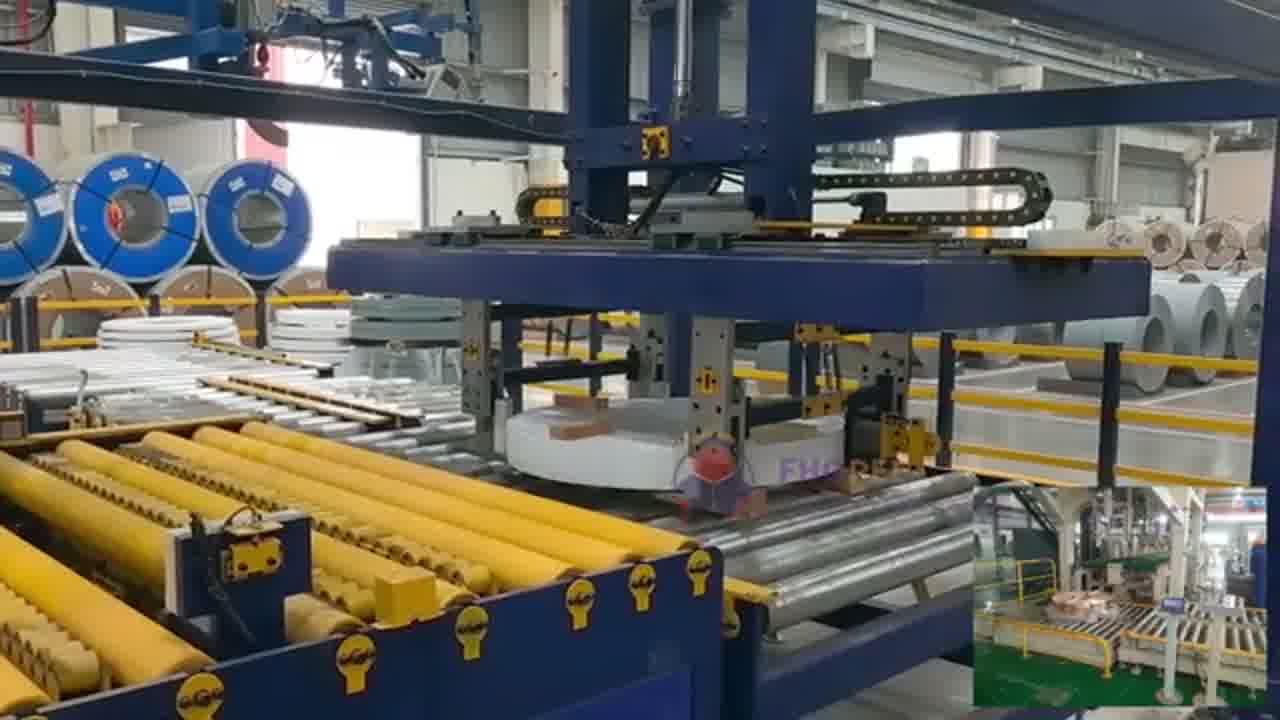 Film-wrapped steel coil on a roller conveyor with a stack of finished coils standing in the background