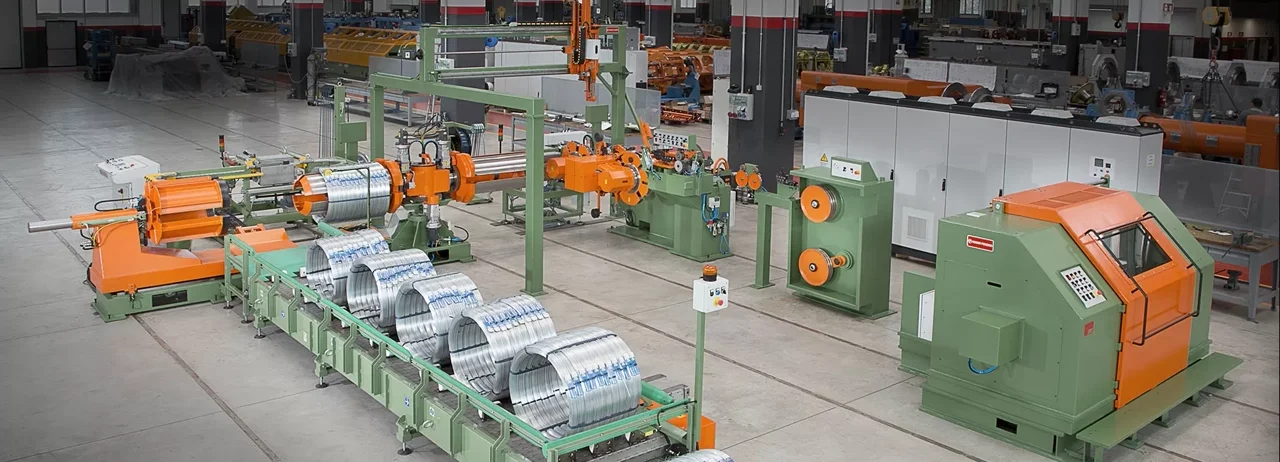 A steel-wire rewinding and coil-compacting line with green machine frames and orange moving parts